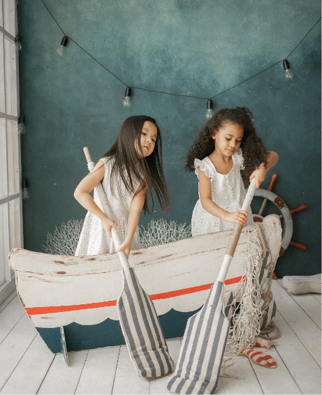  two little girls in white dresses play pretend in a wooden boat