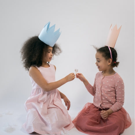  two friends hold flowers together in pink dresses and paper crowns like the dresses they sell at Asdelia Mae Children's Clothing Boutique