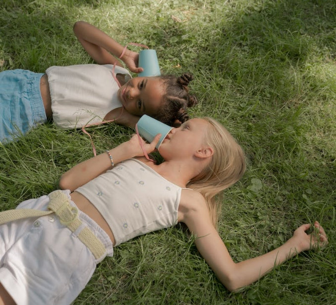  two little girls lay in the green grass playing telephone